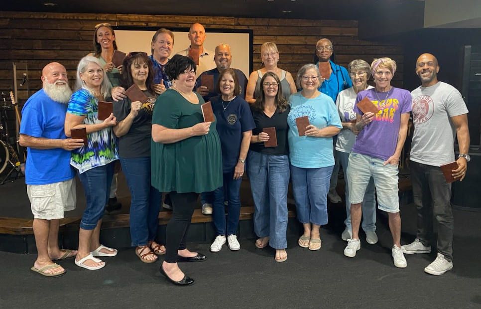 A group of volunteers stands together on a church platform, most of them holding a pocket Bible.