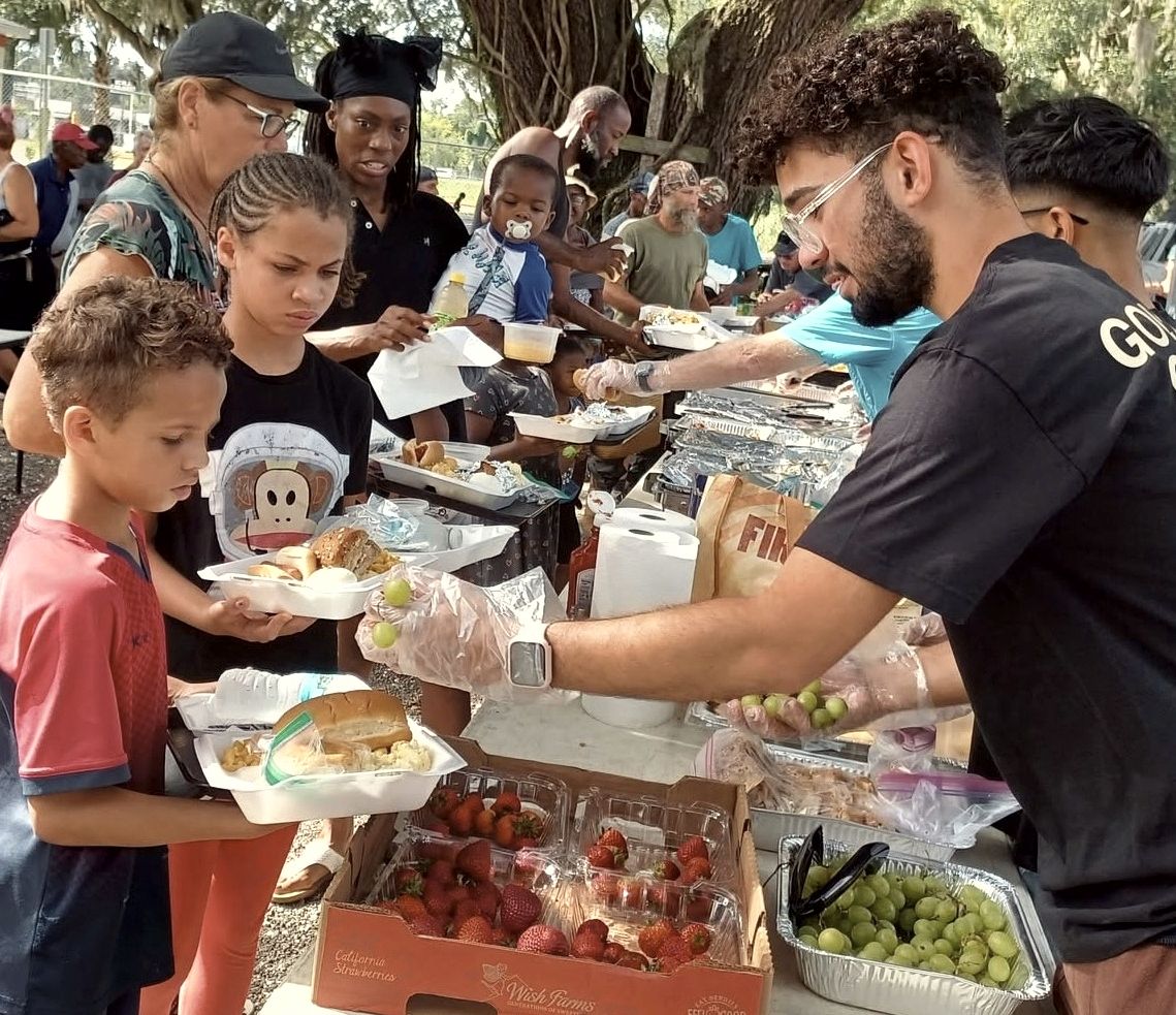 An AFCO 5:20 volunteer serves food to children and families at an outdoor community outreach.