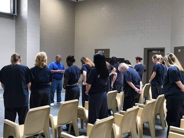 This is a demo of an Adult facility to view the cold environment of incarceration.  Adults stand in a prayer circle between rows of chairs during a jail ministry service.