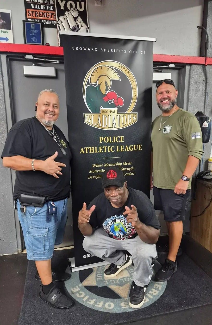 Rick Fernandez with two Police Athletic League leaders beside the BSO PAL Gladiators banner.