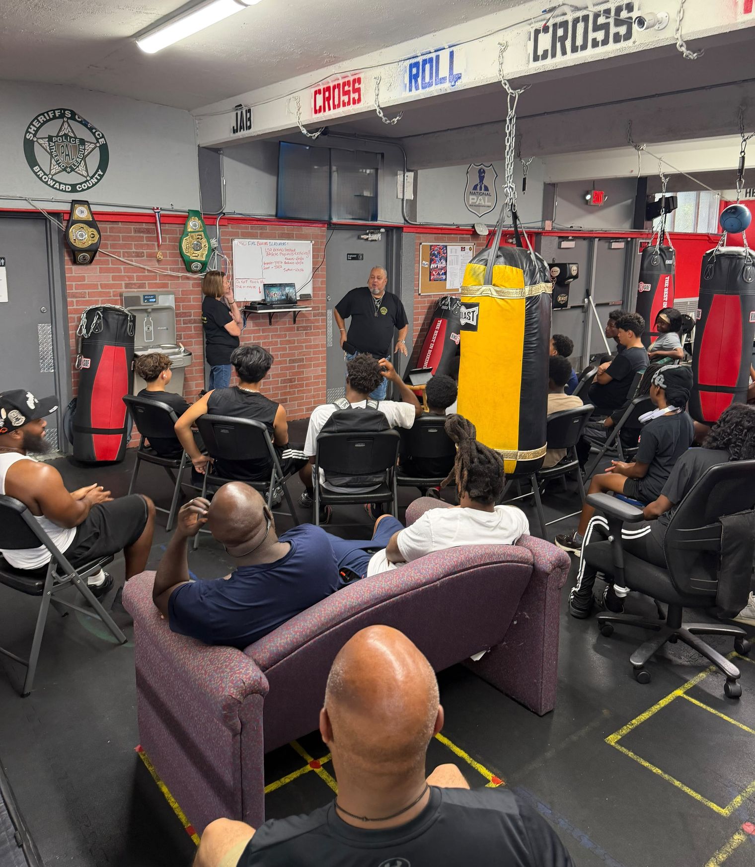 Rick and Donna Fernandez speak to a room of young people seated among the heavy bags at the PAL boxing gym.