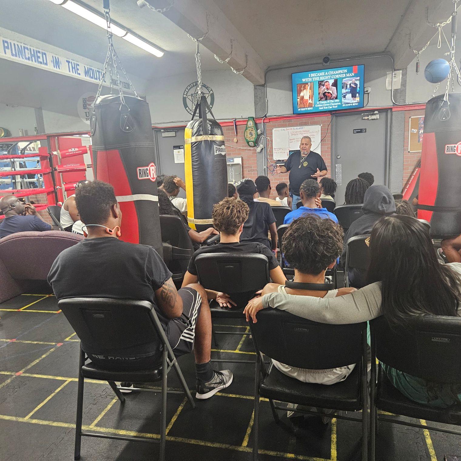 Rick Fernandez speaks beside the ring as the screen reads I became a champion with the right corner man.