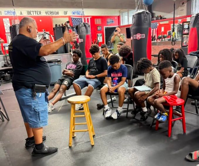 Rick Fernandez prays with a row of young people, heads bowed, at the gym.