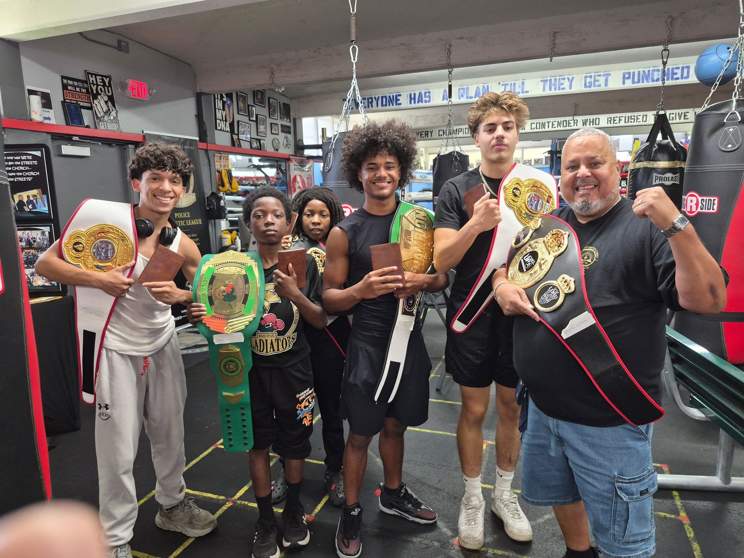 Rick Fernandez celebrates with five young boxers holding championship belts.