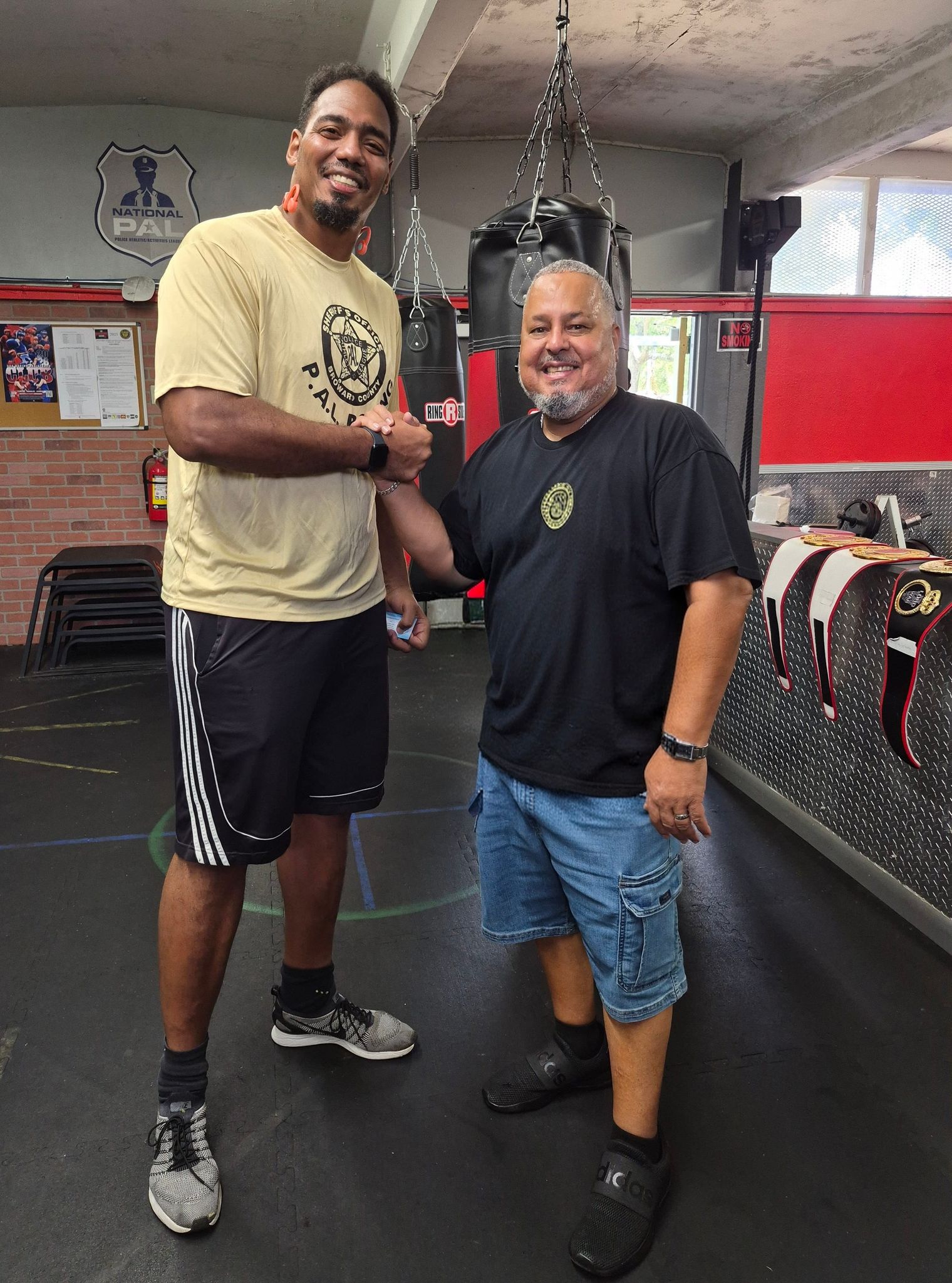 Rick Fernandez clasps hands with a visiting leader beneath the heavy bags at the PAL gym.