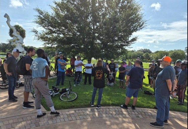 Neighbors and volunteers gather in a circle on the grass at the Ocala park.