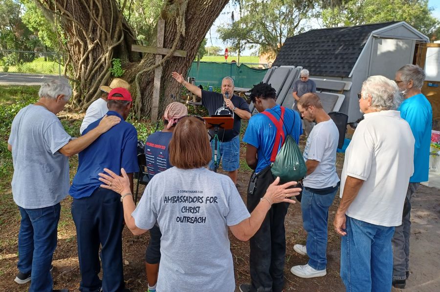 Rick Fernandez raises his arm at the altar call beneath the wooden cross as neighbors bow their heads and lay on hands.